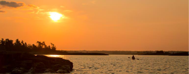 A person kayaking on the water during a sunset.