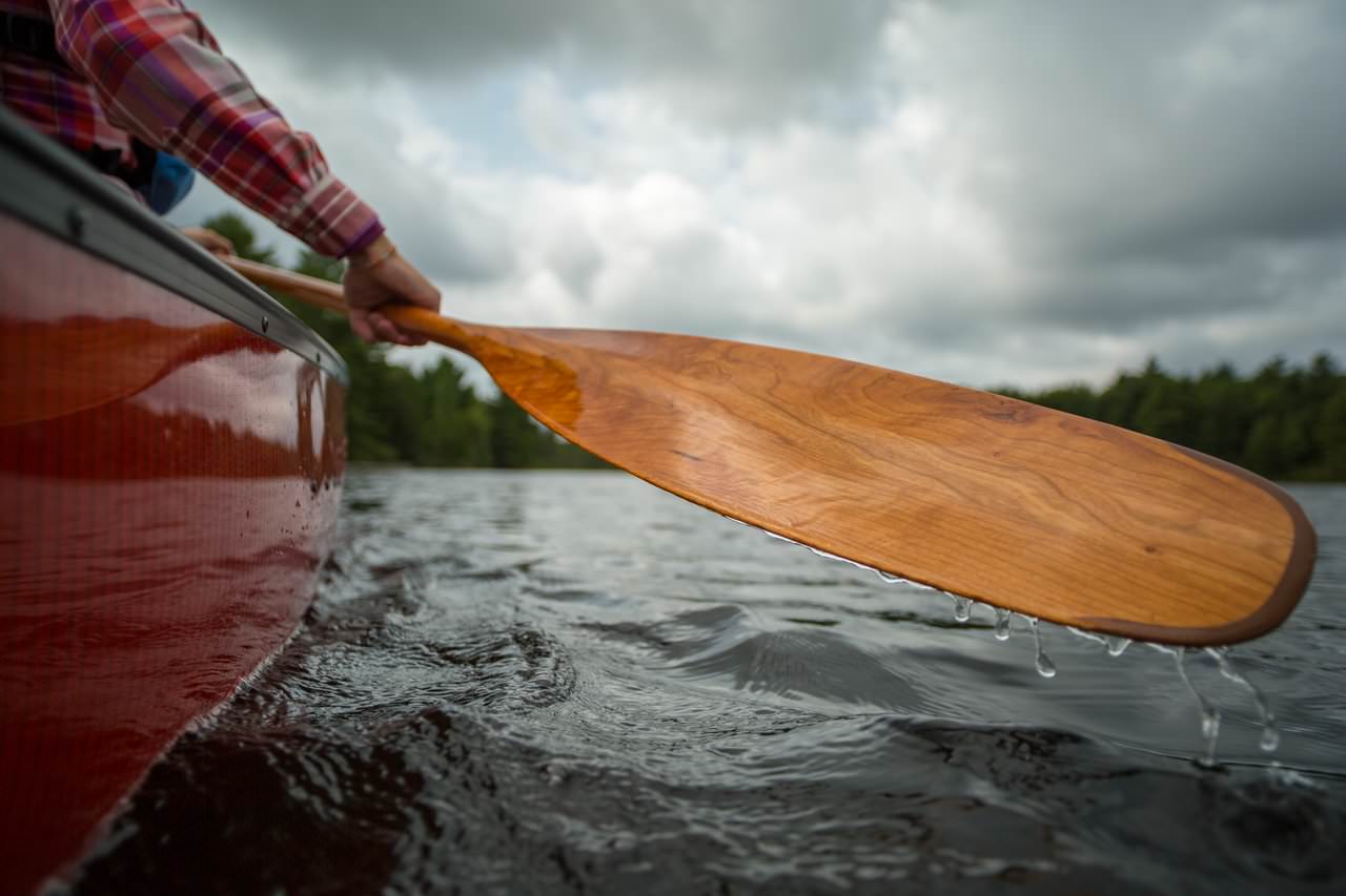 Close up of the arm of a person with a wooden paddle in a canoe on a lake