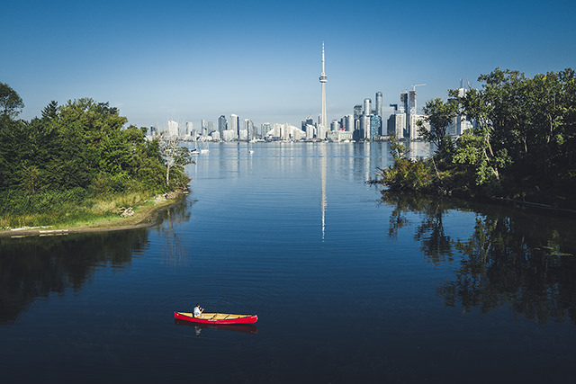 Red canoe paddling through islands with the city of Toronto in the background