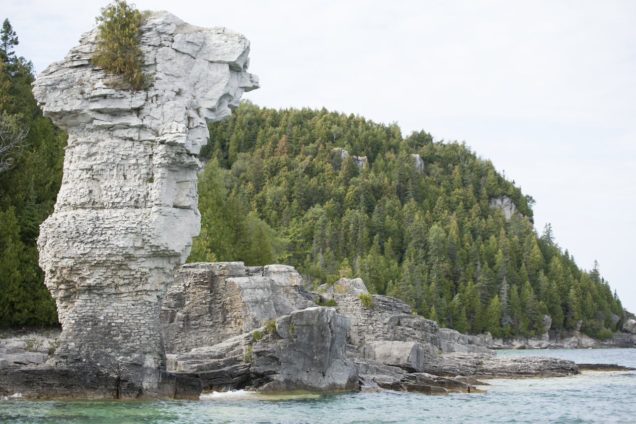 Une formation rocheuse géante semblable à un grand pot de fleurs, entourée d'un lac et d'une forêt