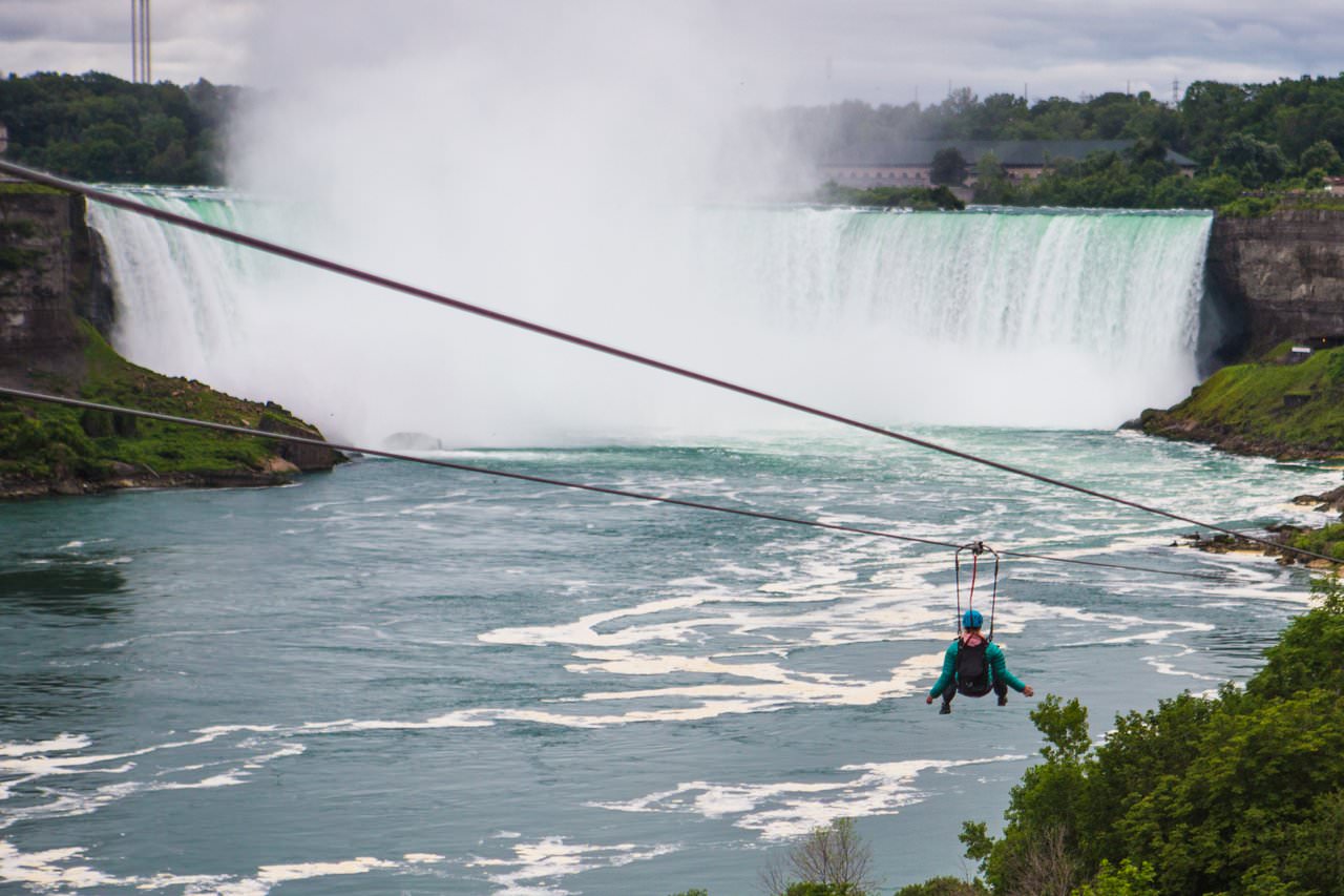 Aerial view of a person descending a zipline against the backdrop of Niagara Falls