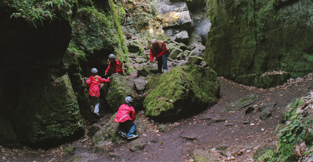 Four people dressed in red jackets are exploring the bottom of a cave