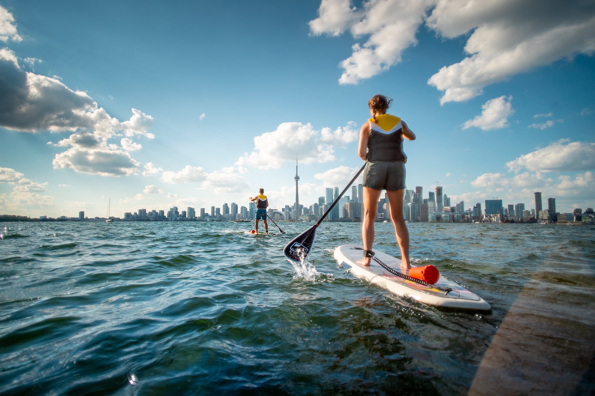 Deux personnes sur des planches à pagaie debout, sur l'eau à l'approche de l'horizon de la ville de Toronto