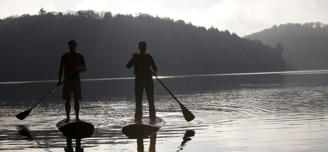 Silhouettes of two men stand up paddling in the water.