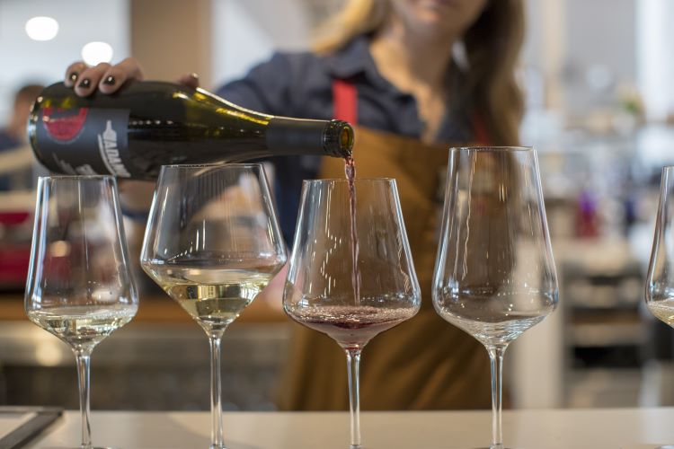 A person pouring wine into a wine glass beside three other glasses.