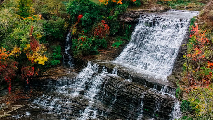 Wasser stürzt einen Wasserfall hinunter, umgeben von Herbstfarben