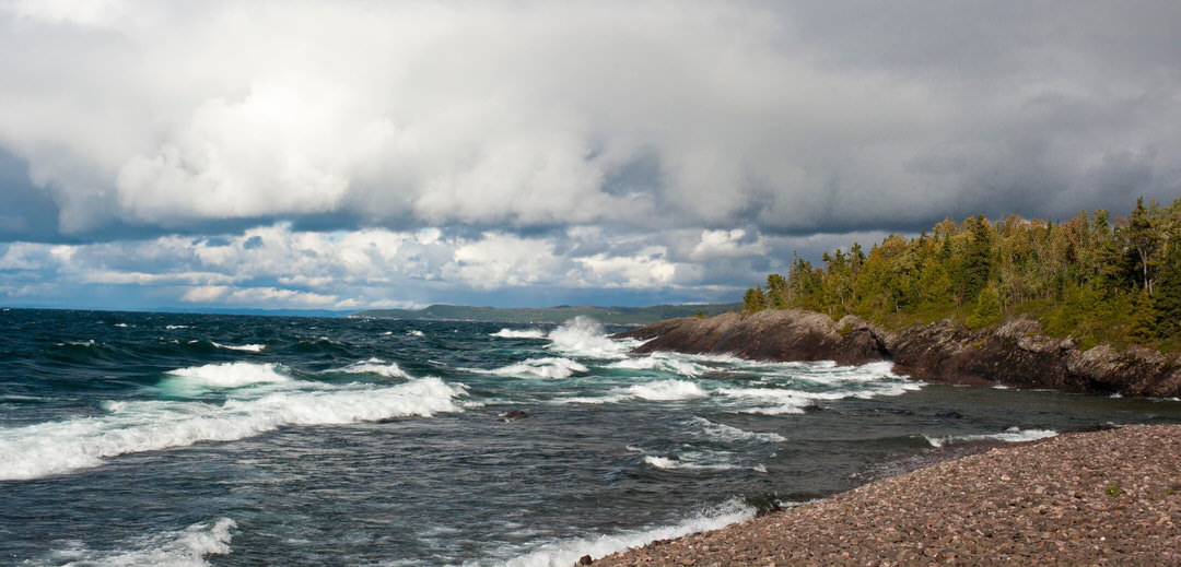 Rough waves crashing along a rocky shore as stormy clouds slowly roll in over the water