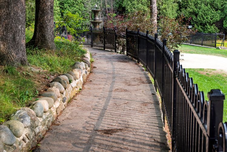 A stone pathway with a fence leads to a fountain. 