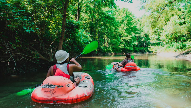 Two people paddling along a river surrounded by lush greenery. 