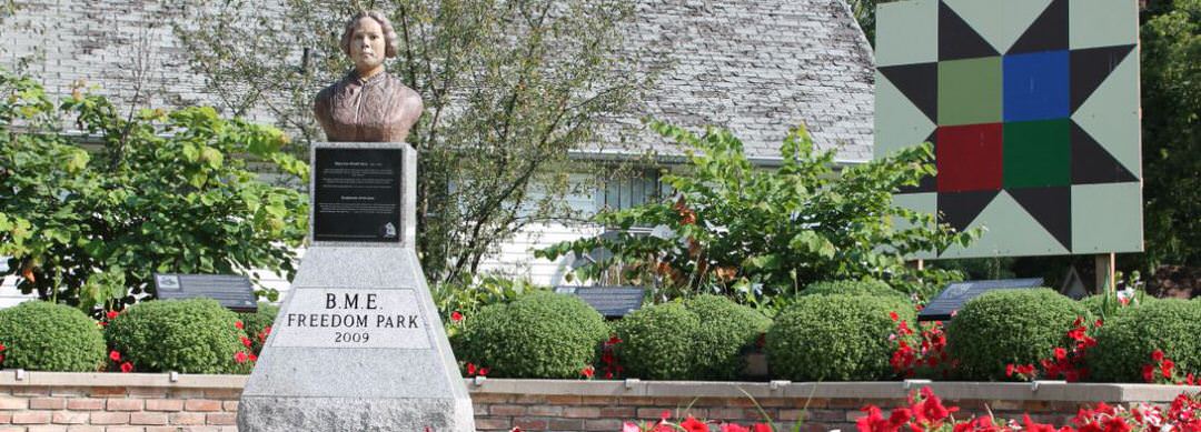 A bust on a pedestal, commemorating freedom; surrounded by gardens and standing tall is a large geometric shape artwork