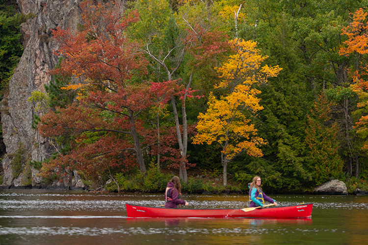 Cliffs overlook a serene lake at dusk with one lone kayaker.