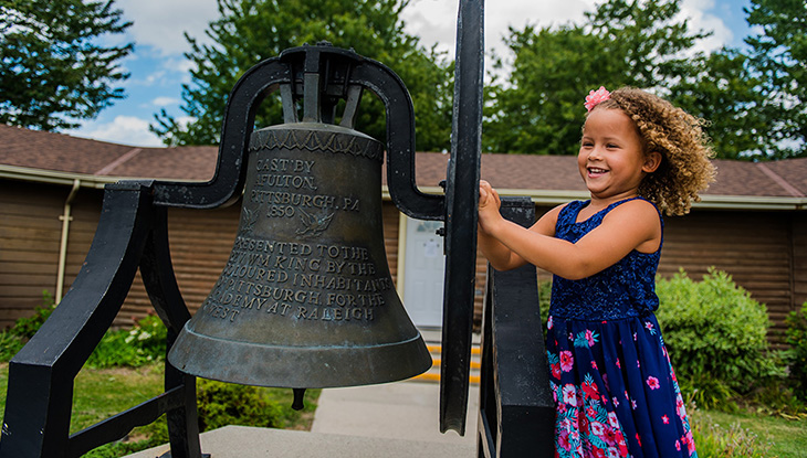 A little girl gleefully ringing a bell