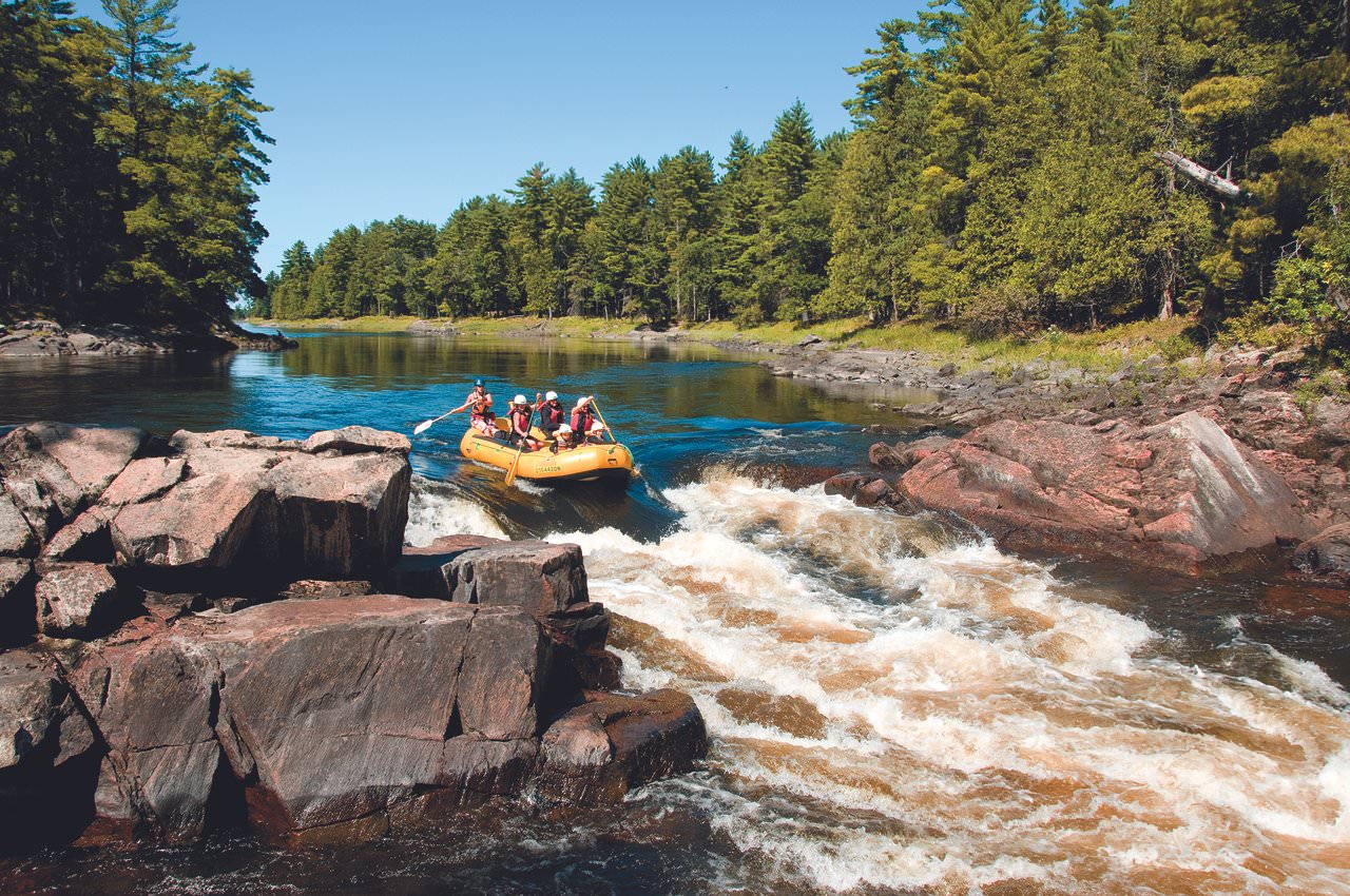 A group of people in a yellow raft going down a small waterfall