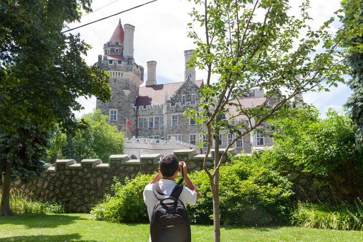 Un homme prend une photo de Casa Loma entourée de verdure.