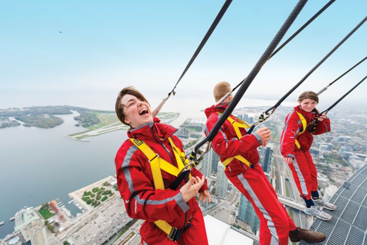 Three people walking along the CN Tower EdgeWalk with harnesses.