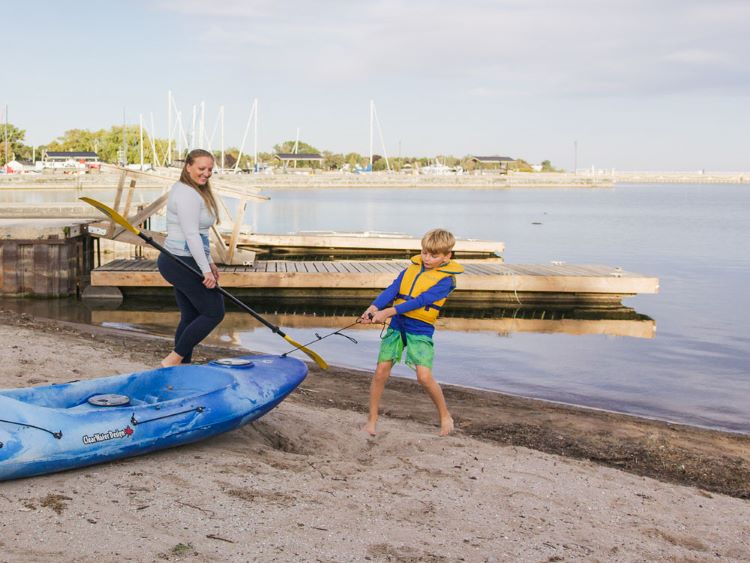 Un jeune garçon tire un kayak bleu sur la plage de Cobourg en direction de l’eau.