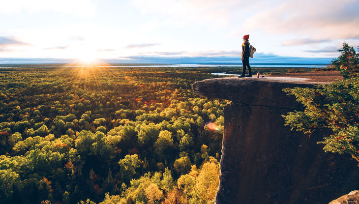 Une femme se tient sur un affleurement rocheux surplombant un paysage pittoresque aux couleurs de l'automne