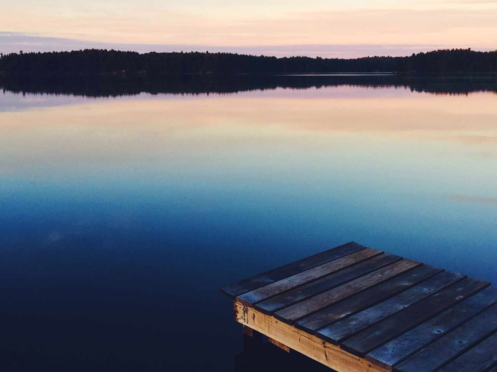 A wooden dock on a calm lake at sunset.