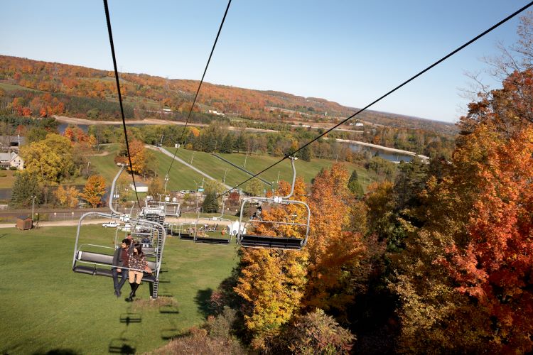 Two people riding in a chairlift surrounded by fall colours.