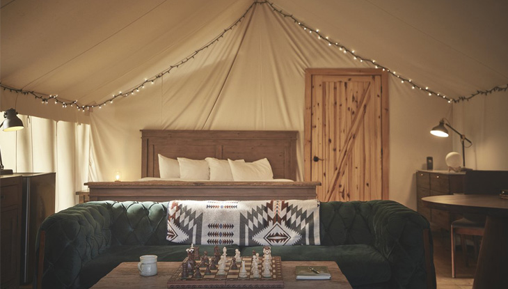 A chessboard on a table in front of a chair and bed