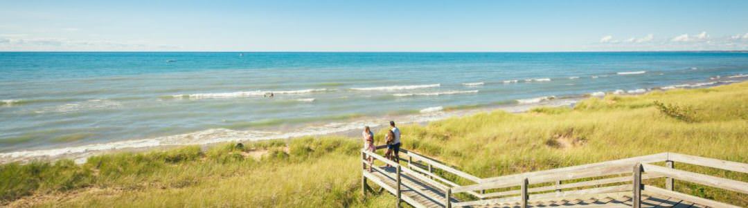 Un homme et une femme se tiennent au sommet d'un point de vue, regardant les vagues de la plage bleue