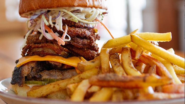 A tall hamburger with fries on a plate.