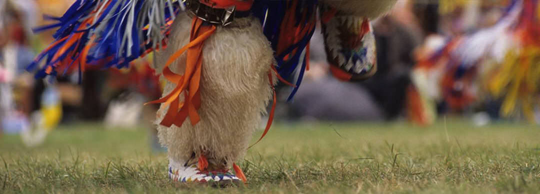 Close up view of an Indigenous dancer’s feet at a Pow Wow, adorned in colourful traditional attire