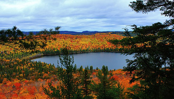 View of a lake surrounded by red, orange and green fall foliage.