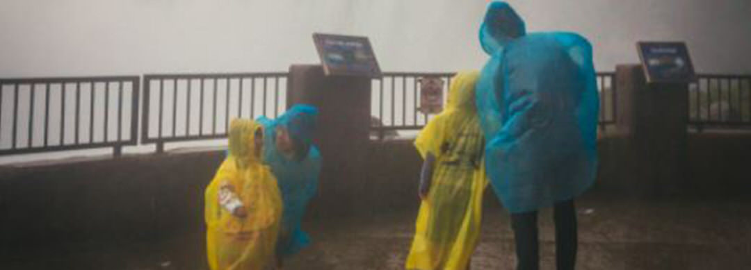 A group of people in rain poncho standing in front of the railing, while mist from Niagara Falls sprays