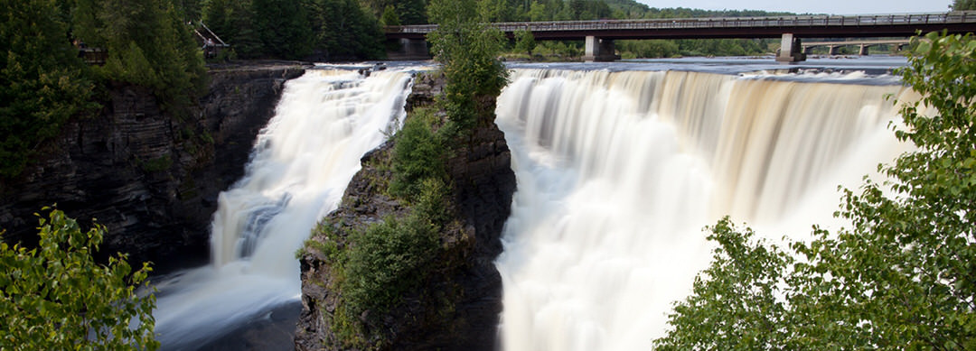 Eau qui se déverse en trombe dans les chutes, avec un pont bas en arrière-plan 