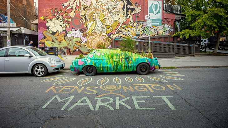 鮮やかな緑色の車の前に、チョークで「Kensington Market」と書かれたストリートアート。