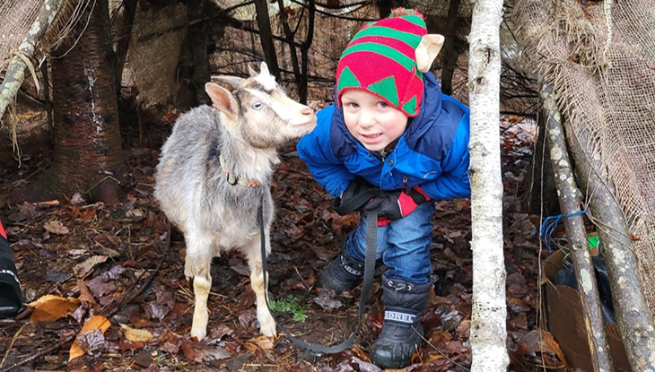 A young boy crouching beside a goat