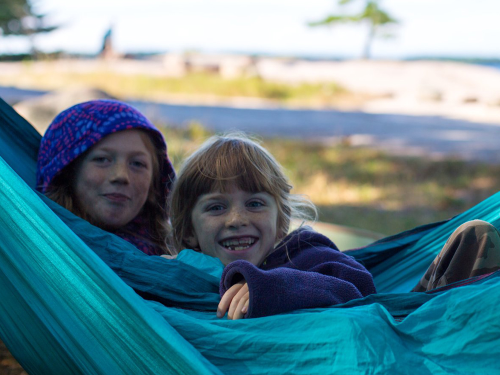 Two young girls peering out from a blue hammock.