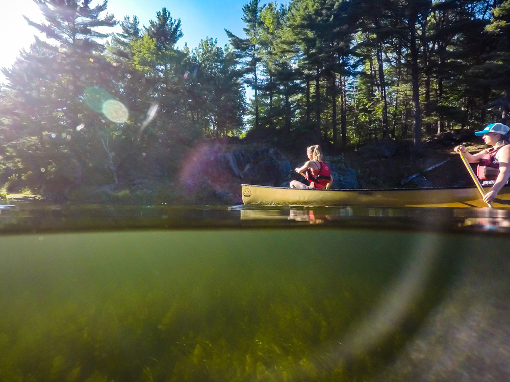 Two women paddle a canoe on a quiet lake.