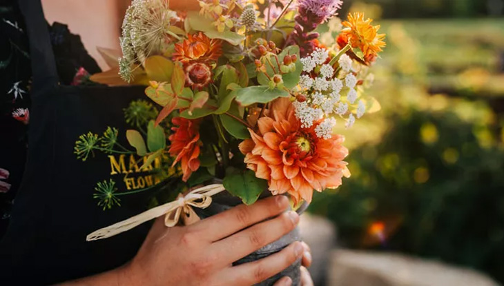 A person holding a freshly cut bouquet of flowers tied with a bow.