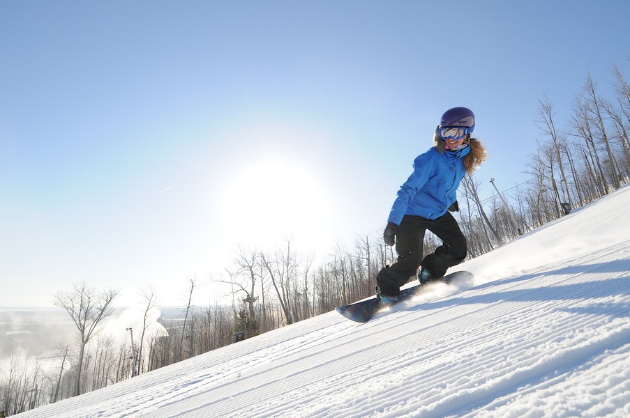 A person snowboarding down a snowy hill under the sunshine.