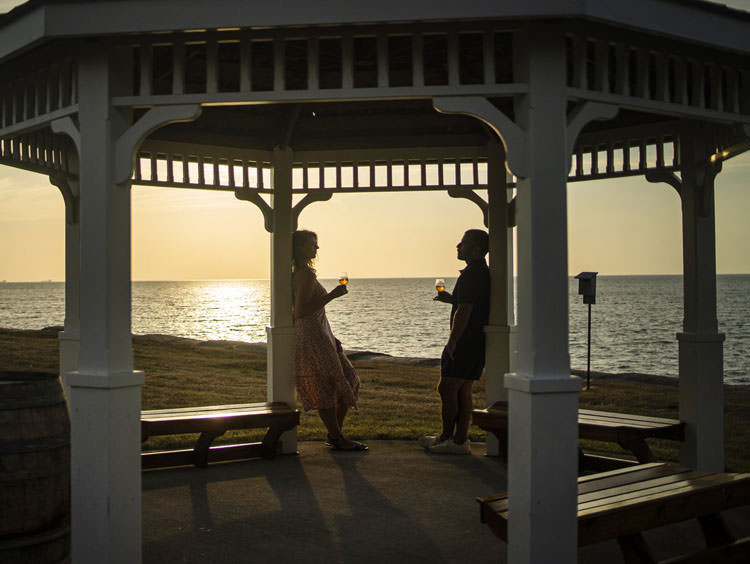 Un hombre y una mujer disfrutando de una copa de vino en un mirador contemplando la puesta de sol sobre el lago