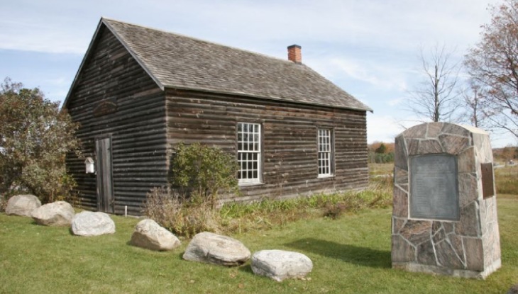 A stone covered plaque beside a historic log building.