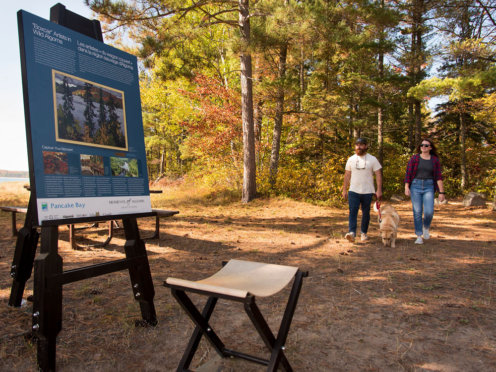 A couple walk towards an informational plaque in a park.