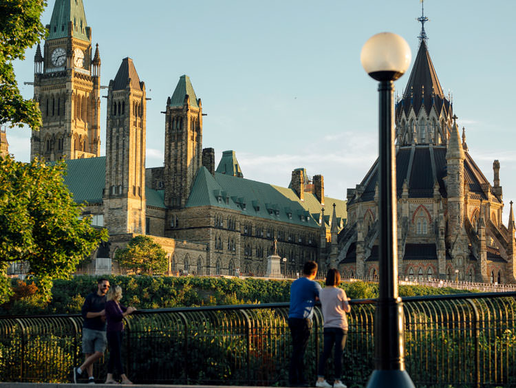 Two people looking at the Parliament Buildings beside a large lamp post.