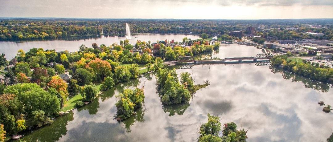 The lake is surrounded by fall-coloured trees with a bridge between 2 land masses.