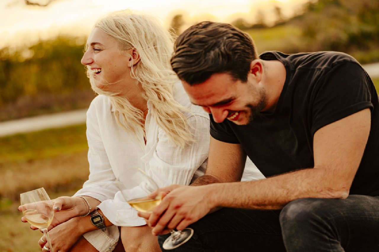 A man and woman laughing together with a glass of wine in hand.