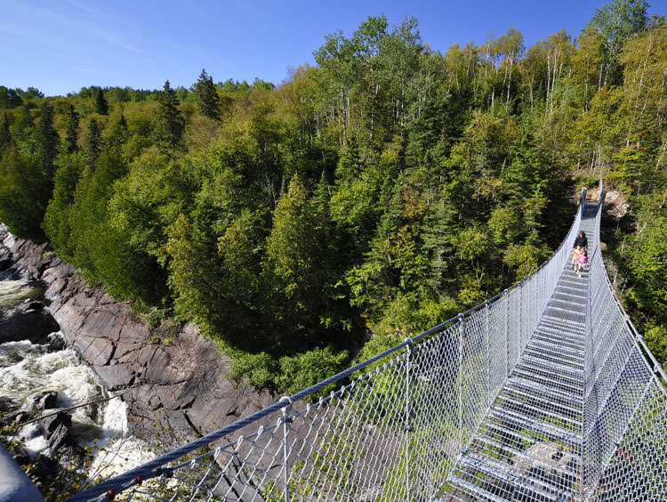 Eine Person und zwei kleine Kinder überqueren eine Hängebrücke