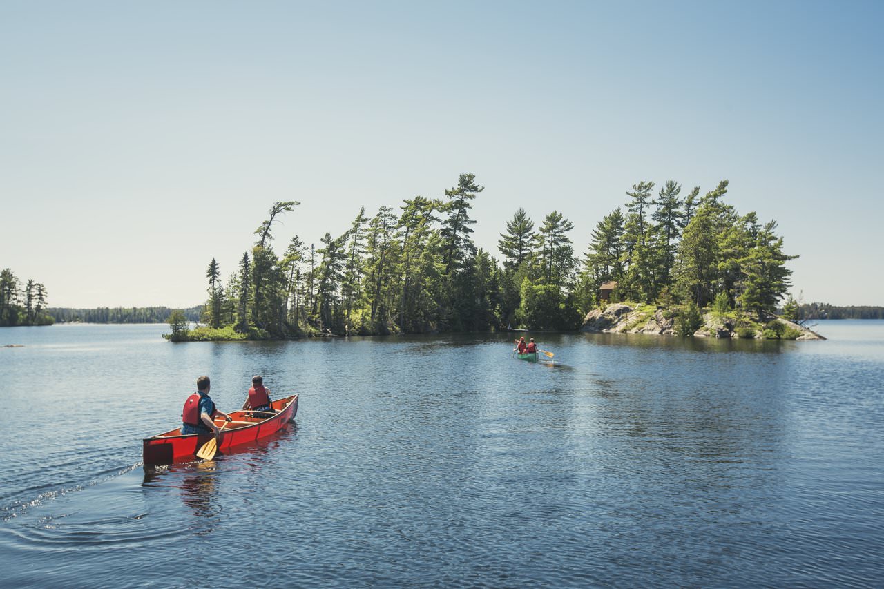 Two people paddling in a red canoe with an island in the background