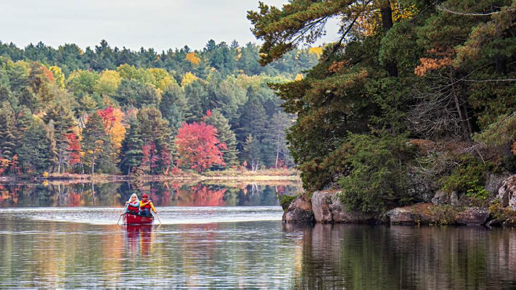 Dos personas navegando en canoa por un lago rodeado de los colores del otoño