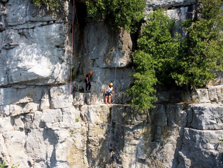 Two rock climbers pause on a ledge of a dramatic rock face.