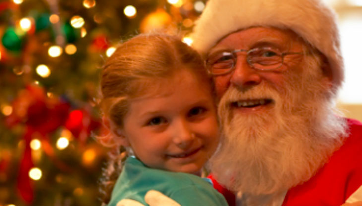 A young child smiles for a photo with Santa Claus.