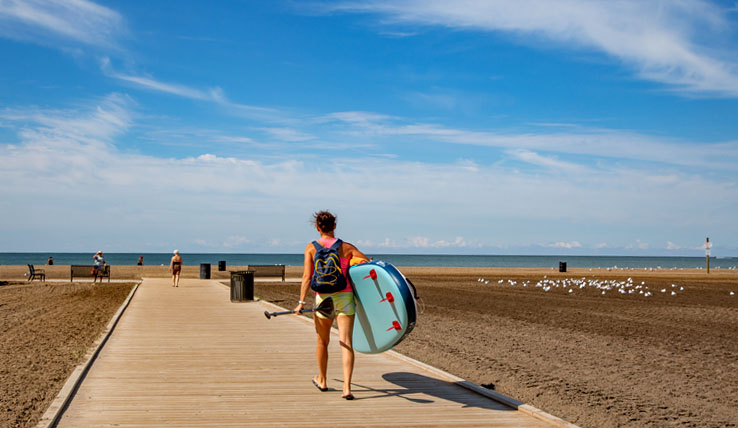 A woman carries a standup paddle board to the beach.