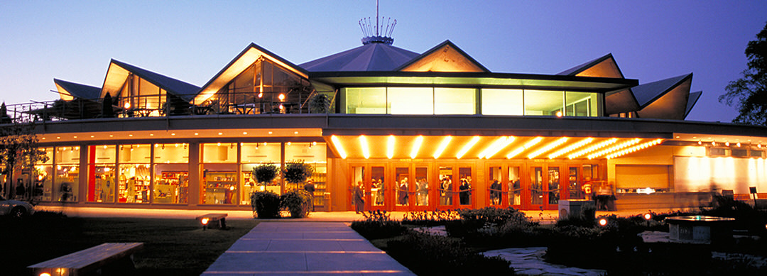 A playhouse filled with sharp-dressed people is lit up brilliantly against a dusky sky.