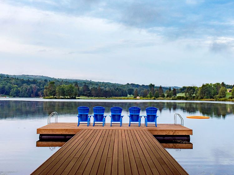 Five blue Muskoka chairs sit at the end of a dock overlooking a beautiful lake at Deerhurst Resort.